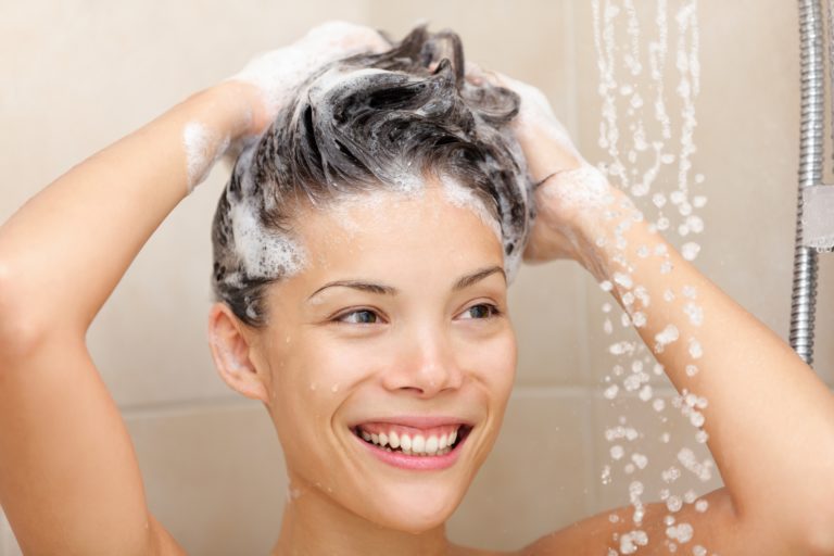 Woman washing hair with shampoo foam in shower smiling happy looking at running warm water