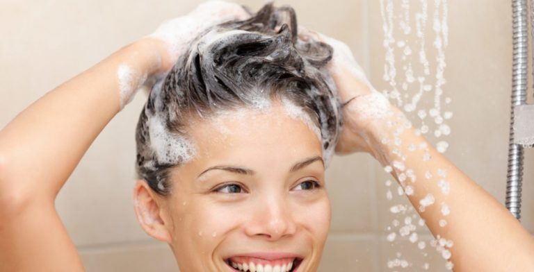 Woman washing hair with shampoo foam in shower smiling happy looking at running warm water