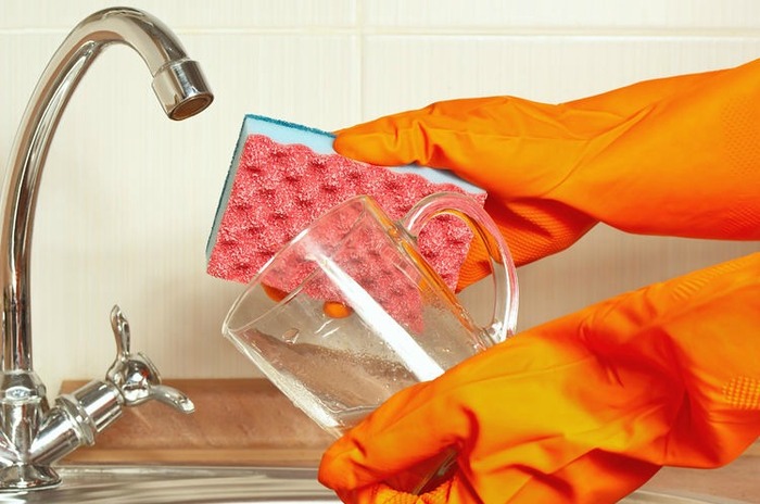 person using cleaning gloves and a sponge to clean hard water build up off of a glass