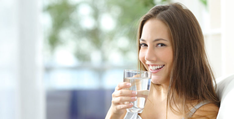 lady that is drinking water at home while sitting on her couch smiling