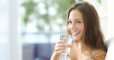 lady that is drinking water at home while sitting on her couch smiling
