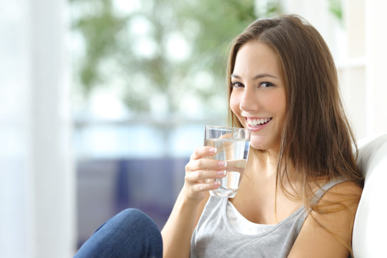 lady that is drinking water at home while sitting on her couch smiling