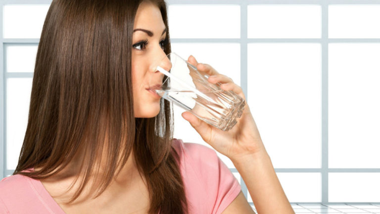 woman drinking water with a bathroom tile back drop