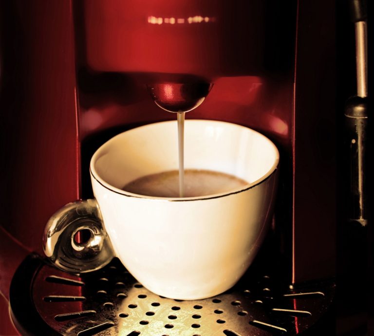 a red coffee machine pouring coffee into a white mug