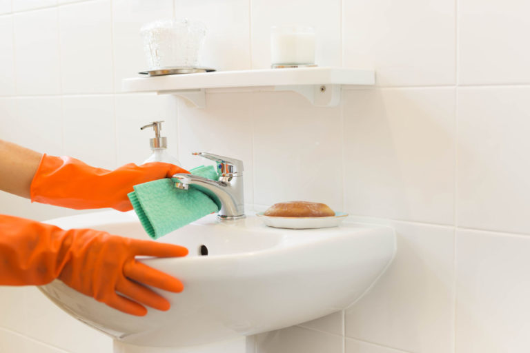 gloved hands attempting to use a sponge to clean hard water residue from a sink