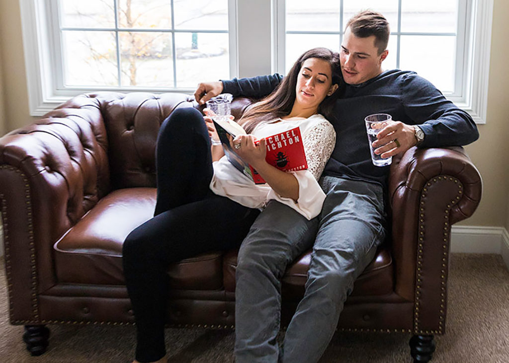 husband and wife drinking glasses of water on the couch while reading a book