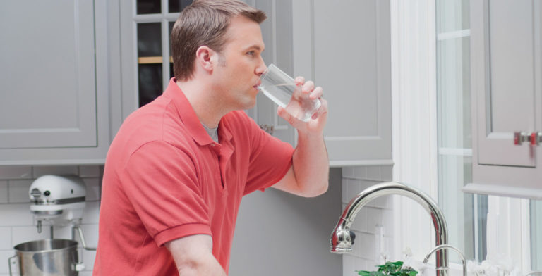 man drinking a glass of water after getting it from the faucet