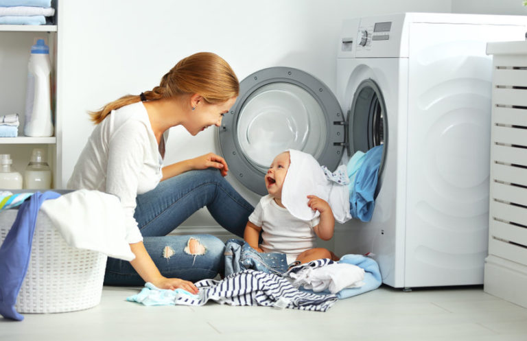 woman unloading her dryer with her baby at her feet smiling