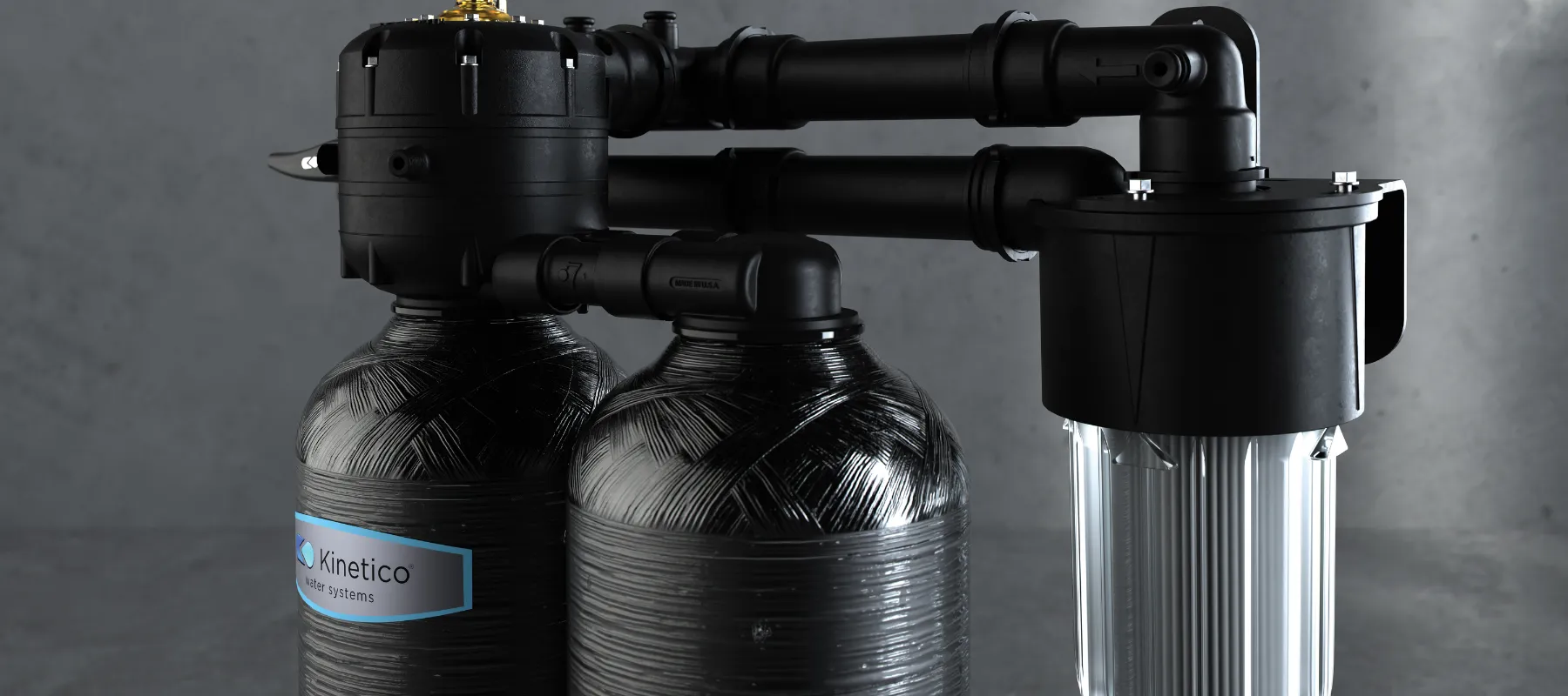 A black dual-tank water filtration system with a transparent cylindrical filter attached to the side, set against a gray background. The tanks are labeled “Kinetico.”.
