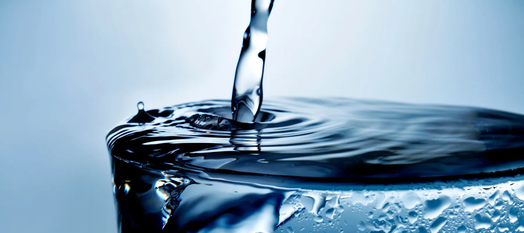 A close-up of water being poured into a clear glass, causing ripples and bubbles on the surface, with cool blue lighting creating a refreshing and clean impression.