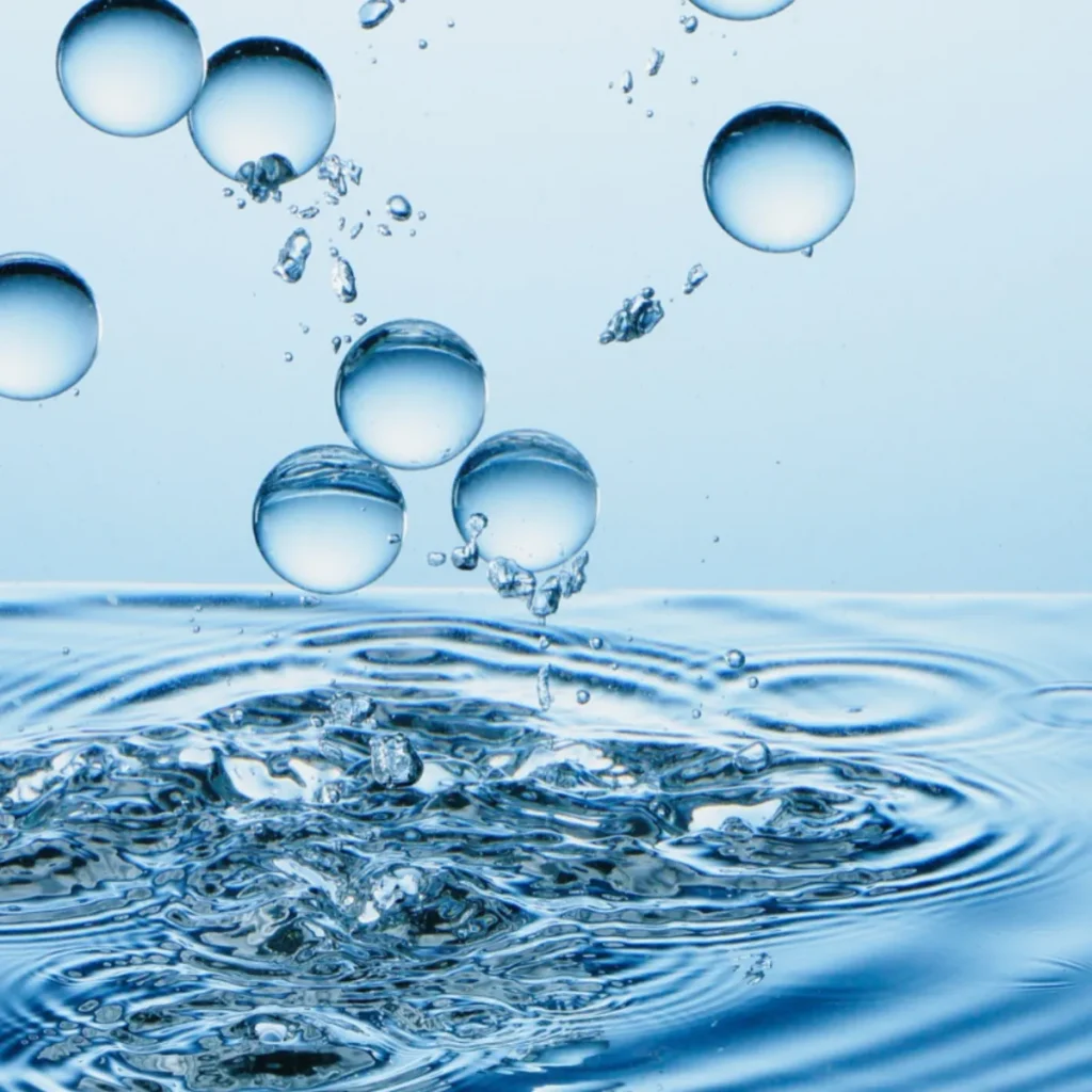 Several water droplets are falling into a clear, rippling pool, causing splashes and waves. The image has a blue tint, giving a fresh and clean feeling.